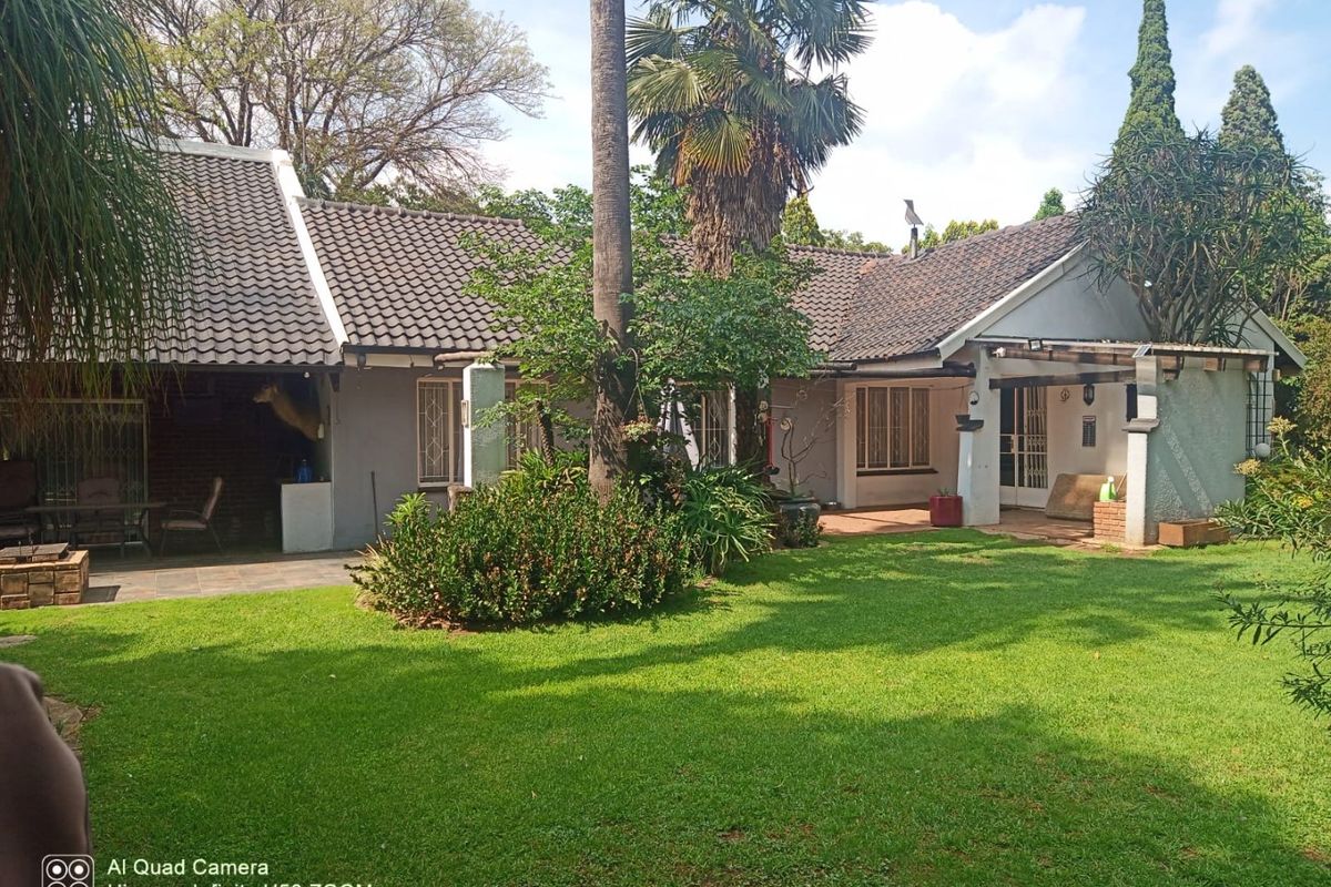 Rear view of the house featuring a spacious lawn, mature trees, and a covered patio area with tiled roofing.