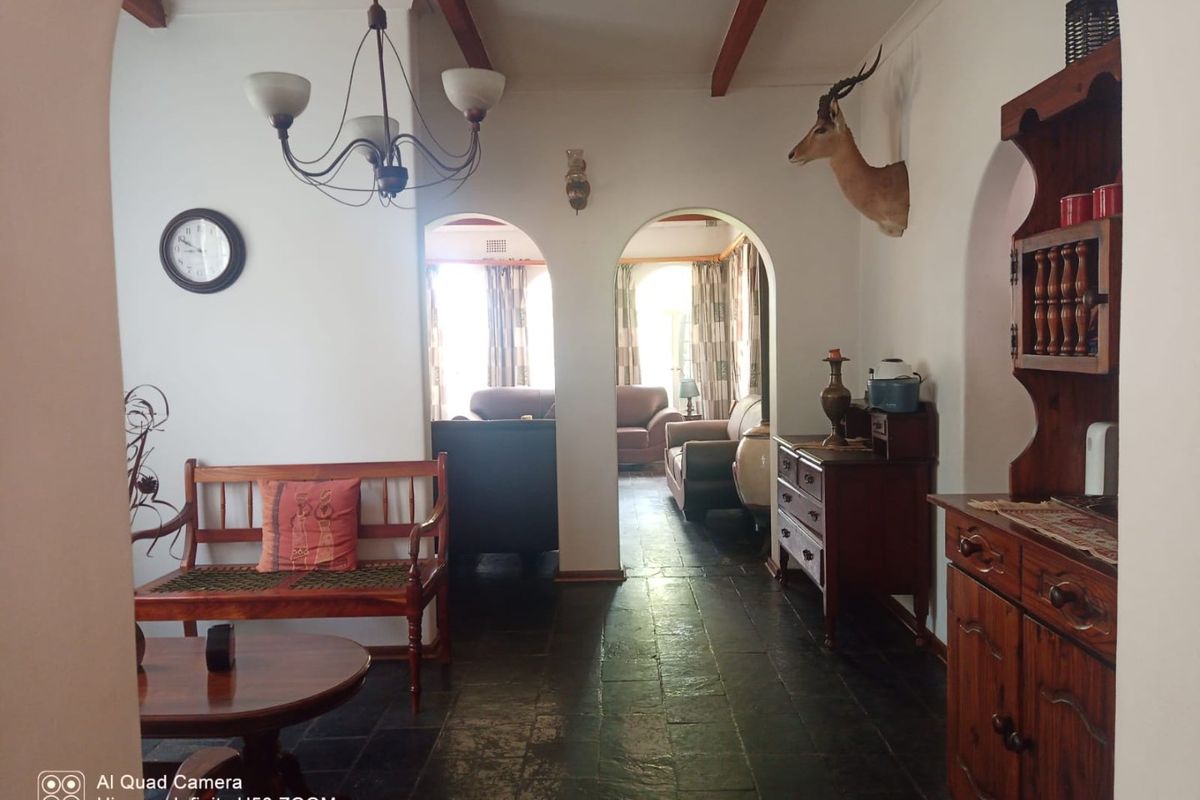 A living area featuring stone tile flooring, exposed timber ceiling beams, and arched doorways leading to an adjacent room.