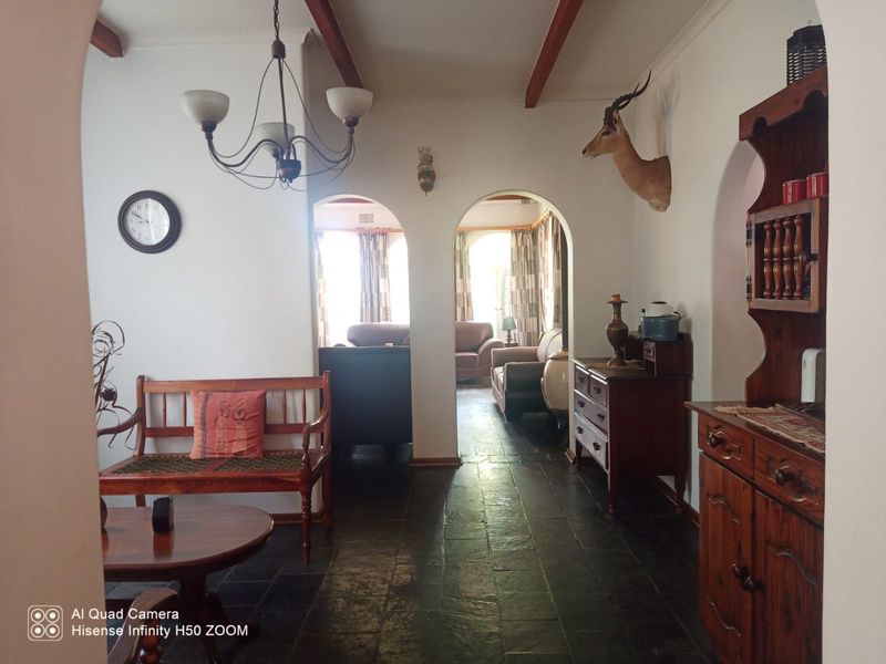 A living area featuring stone tile flooring, exposed timber ceiling beams, and arched doorways leading to an adjacent room.