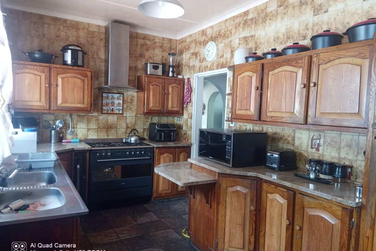 A functional kitchen featuring wooden cabinetry, a gas stove with extractor fan, double basin sink, and tiled finishes throughout.