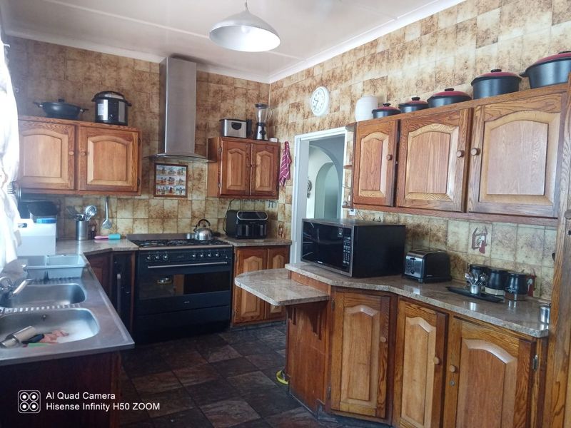 A functional kitchen featuring wooden cabinetry, a gas stove with extractor fan, double basin sink, and tiled finishes throughout.