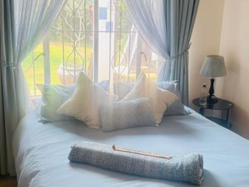 A bedroom featuring a large window with security gate, curtain rails, and an integrated ceiling air vent, providing natural light and garden views.