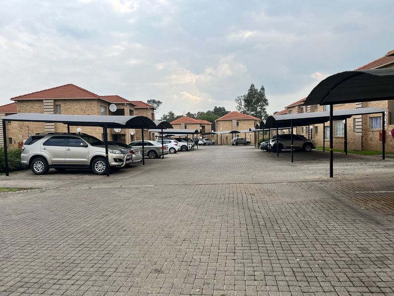 A view of the apartment complex parking area featuring paved driveways and covered carport structures for residents.