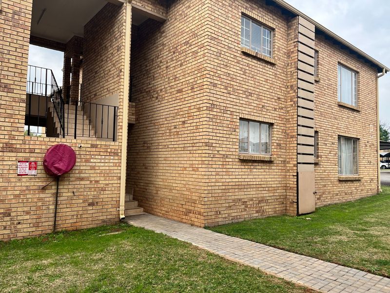 Exterior view of a multi-story apartment building featuring face brick construction, a paved walkway, and an external staircase with metal railings.