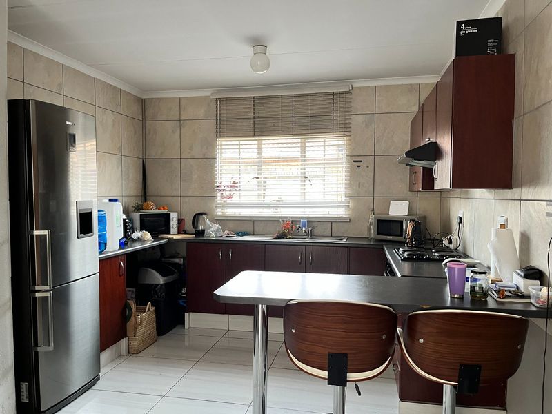 A functional kitchen featuring dark wood cabinetry, tiled walls, a gas hob with extractor, and a breakfast bar area.