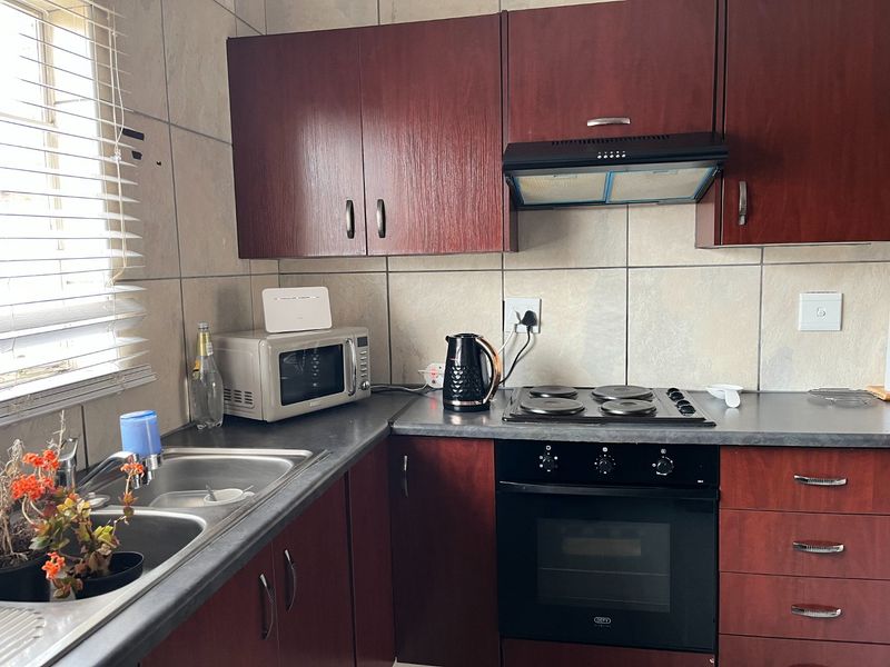 A functional kitchen featuring dark wood-finish cabinetry, a built-in oven with hob, extractor fan, and a double bowl sink with tiled backsplash.