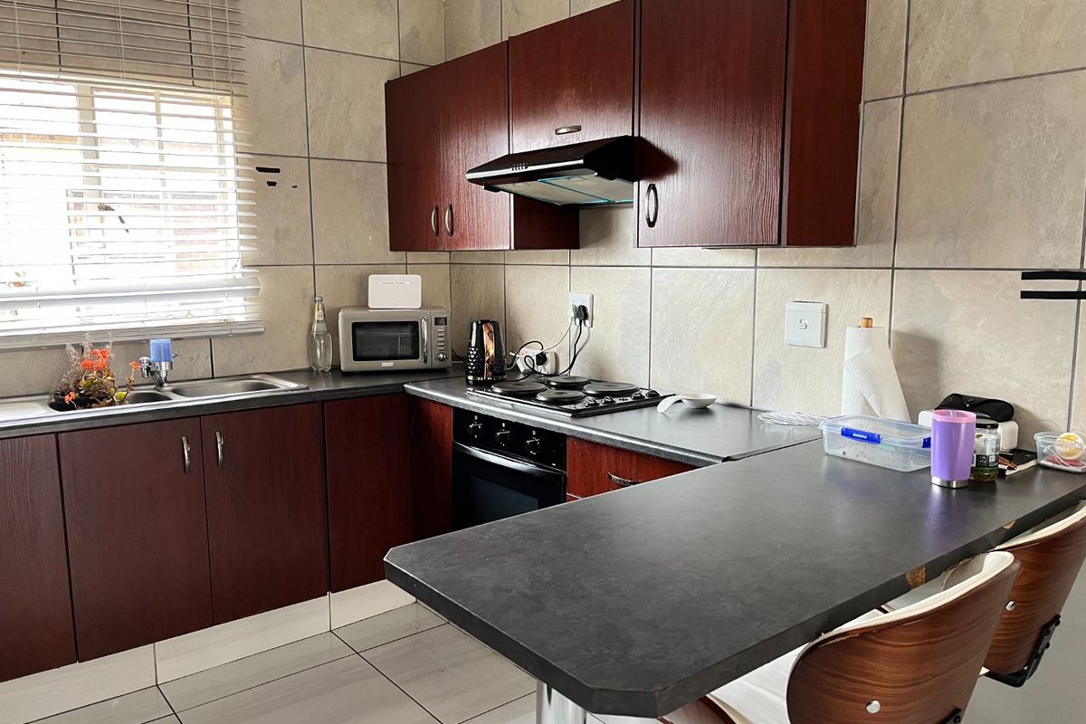A functional kitchen featuring dark wood cabinetry, laminate countertops, a built-in oven with hob, and tiled finishes throughout.