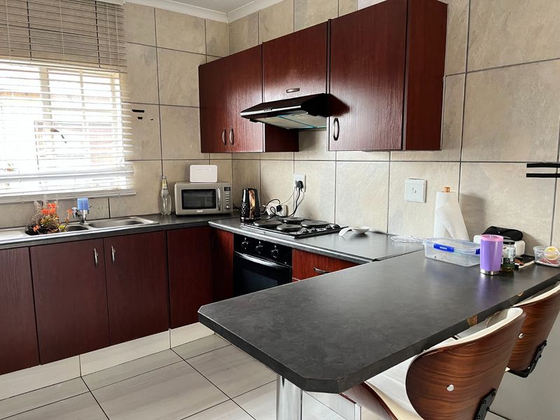 A functional kitchen featuring dark wood cabinetry, laminate countertops, a built-in oven with hob, and tiled finishes throughout.