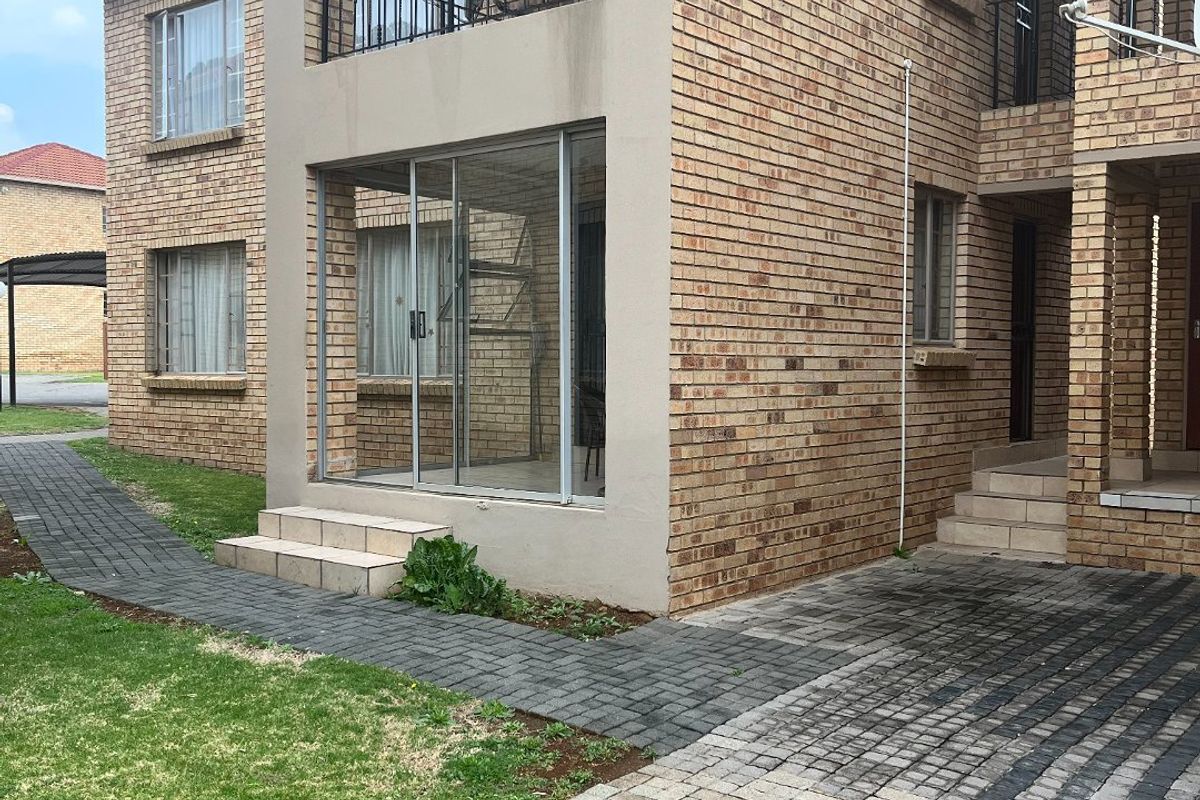 Rear view of a face brick apartment building featuring a ground-floor sliding door entrance, a private balcony, and paved access paths.