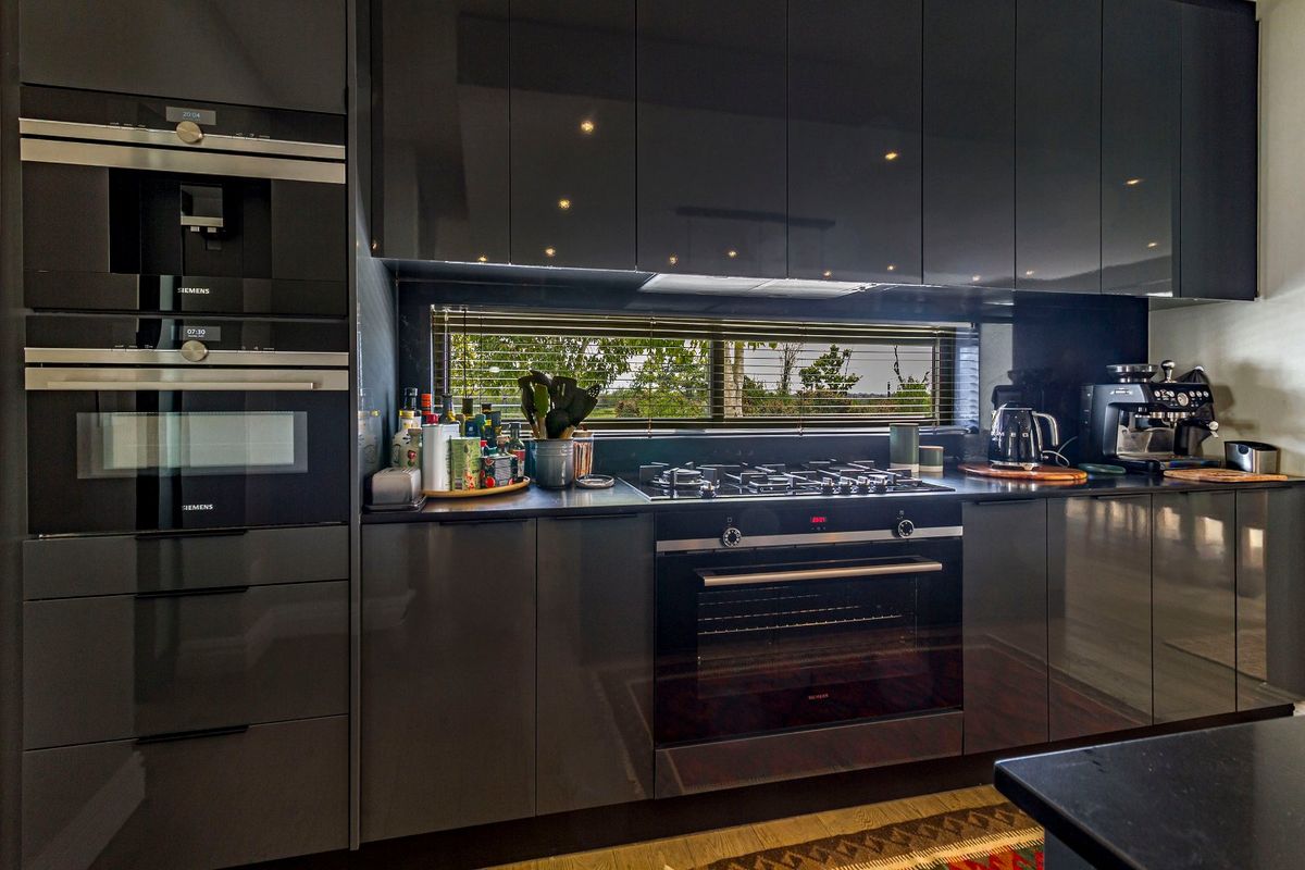 Modern kitchen featuring high-gloss dark cabinetry, integrated Siemens appliances, gas hob, and stone countertops with a sleek, contemporary finish.