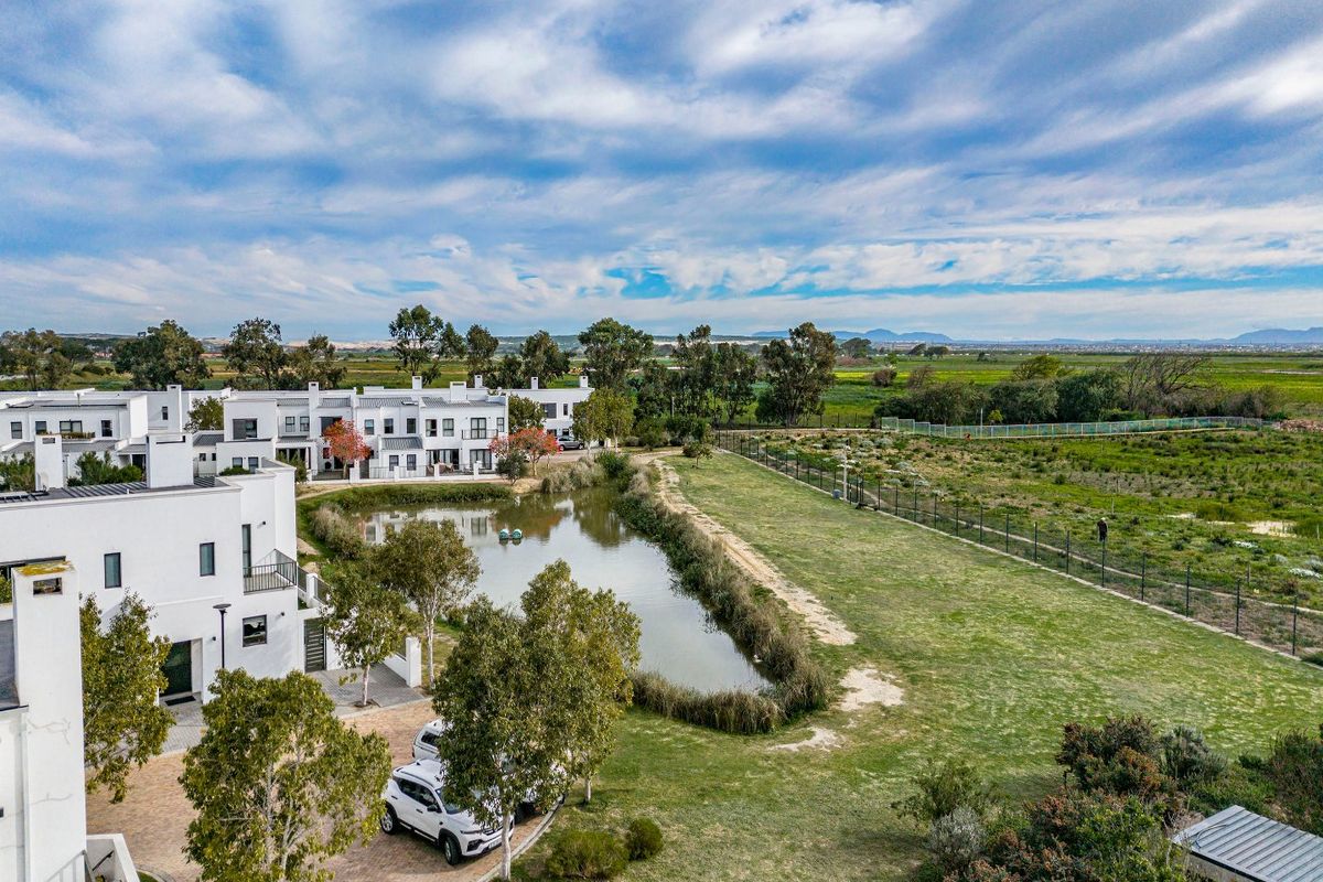 Aerial view of the residential estate featuring a central pond, paved driveway, and surrounding landscaped green spaces with distant mountain views.