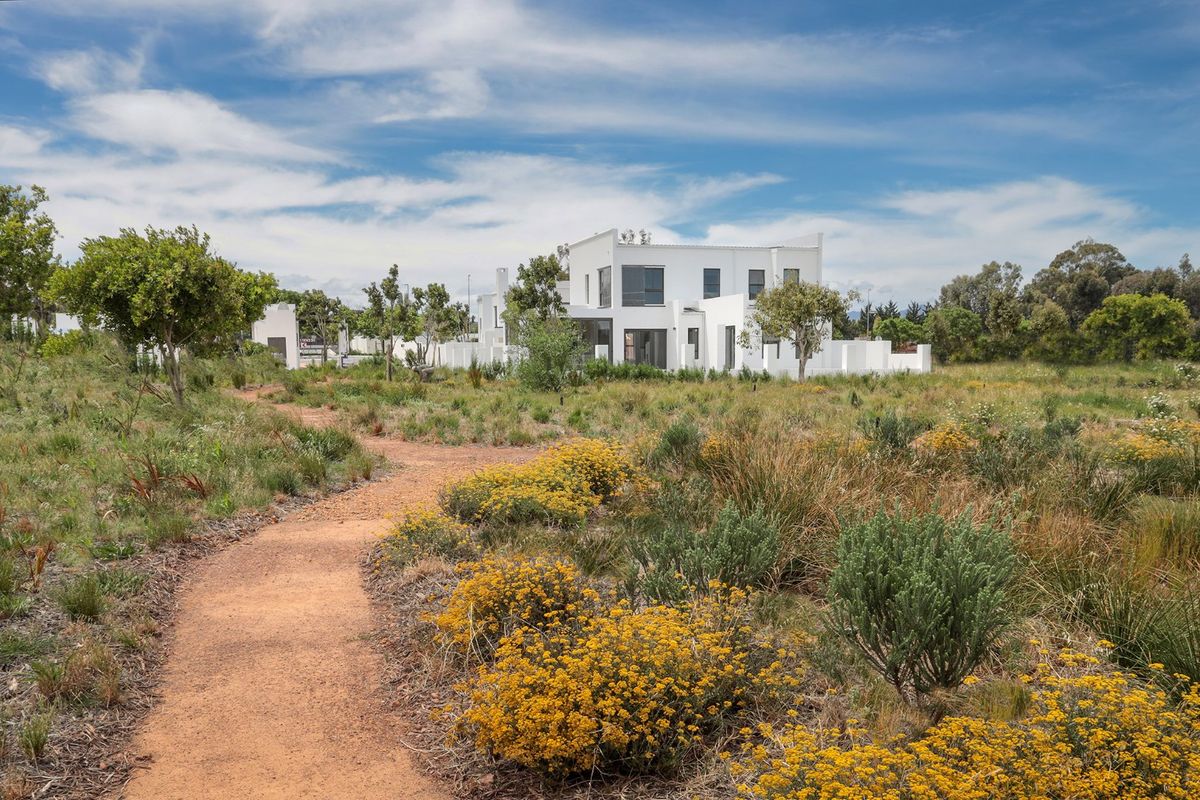 A view of a modern white residential property set within a natural, landscaped garden with a winding pathway.