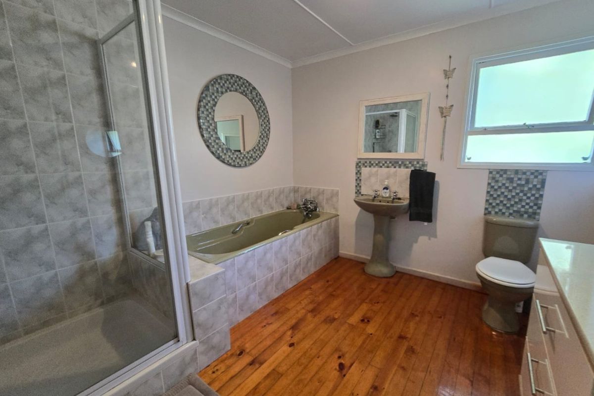 A functional bathroom featuring a separate shower, bathtub, pedestal basin, and toilet, finished with timber flooring and tiled accents.