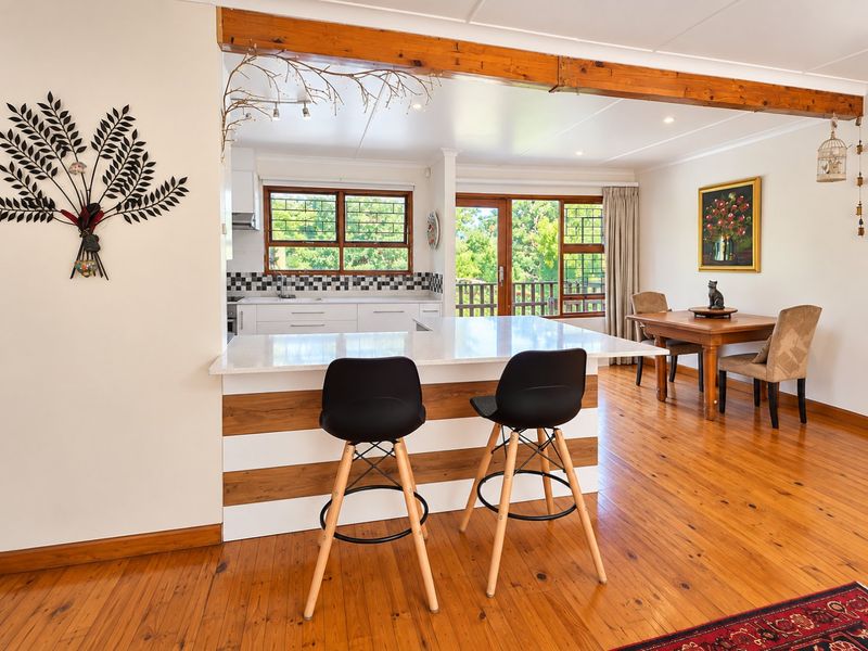 Open plan kitchen and dining area featuring polished timber flooring, a central island with quartz countertop, and direct access to an outdoor balcony.