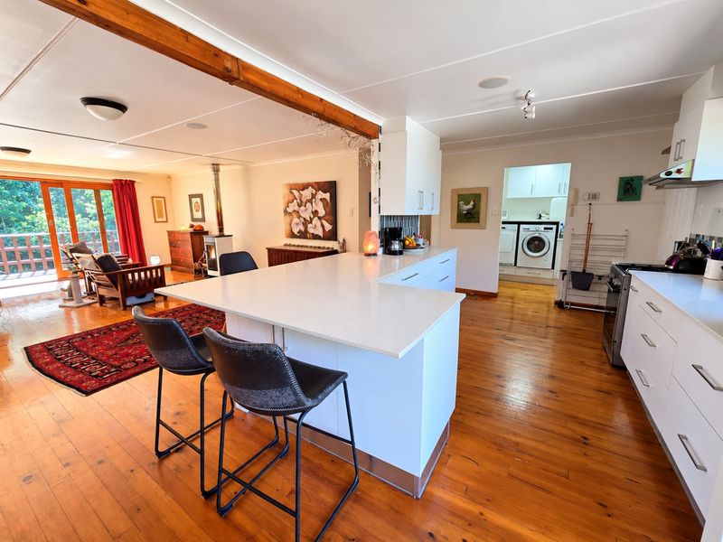 Spacious open-plan kitchen and living area featuring a central island, modern cabinetry, hardwood floors, and a cozy fireplace with access to an outdoor deck.