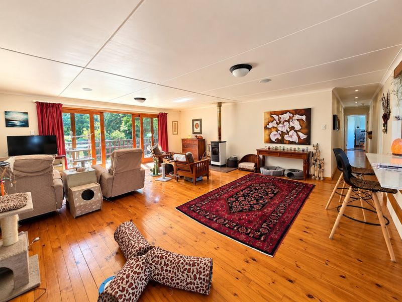 Spacious open-plan living area featuring polished timber flooring, a wood-burning stove, and large sliding glass doors providing access to the outdoor deck.