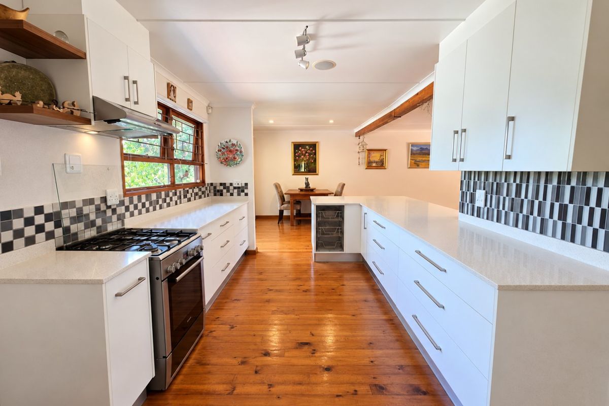 Modern kitchen featuring white cabinetry, quartz countertops, gas stove, extractor fan, and warm timber flooring, leading into an open-plan dining area.