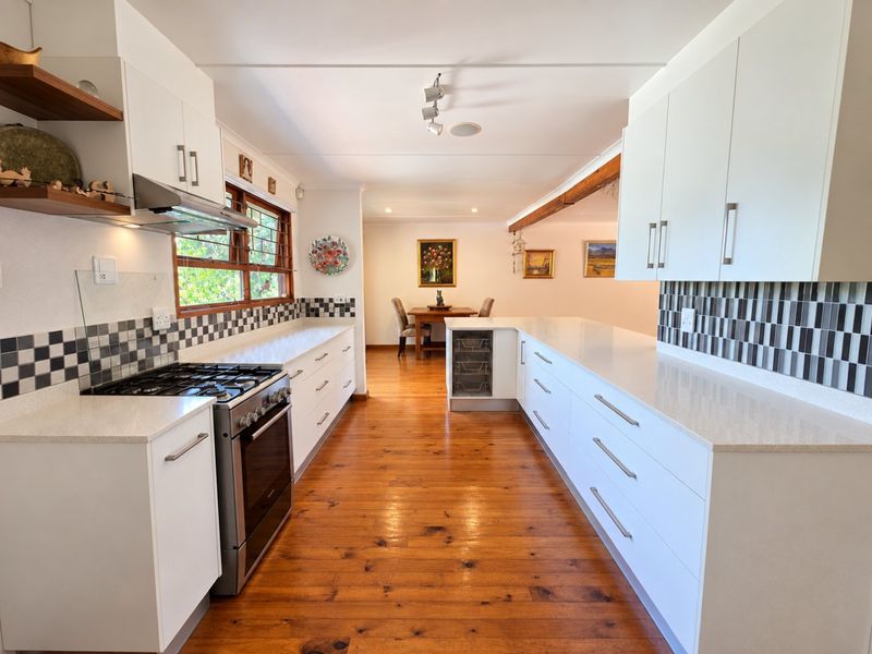 Modern kitchen featuring white cabinetry, quartz countertops, gas stove, extractor fan, and warm timber flooring, leading into an open-plan dining area.