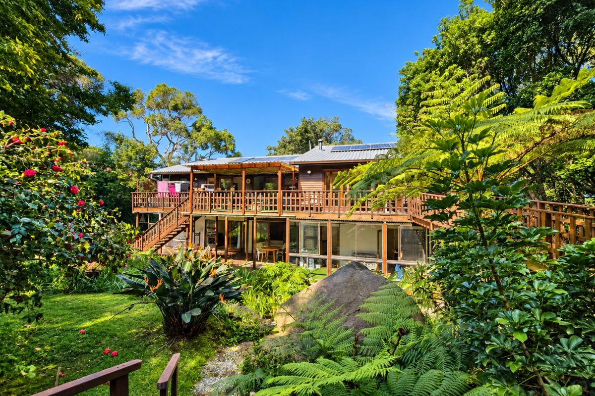 Rear view of a multi-level timber house featuring extensive decking, a staircase, and a lush, landscaped garden setting.