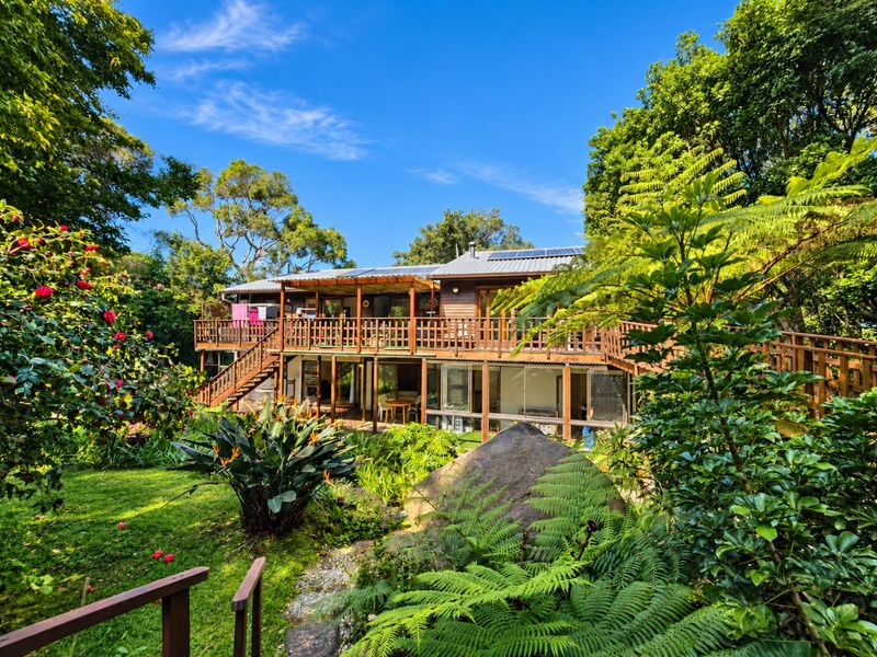 Rear view of a multi-level timber house featuring extensive decking, a staircase, and a lush, landscaped garden setting.