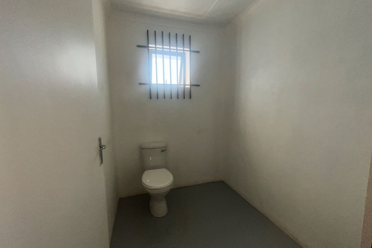 A basic industrial-style restroom featuring a single toilet and a small window secured with metal bars.