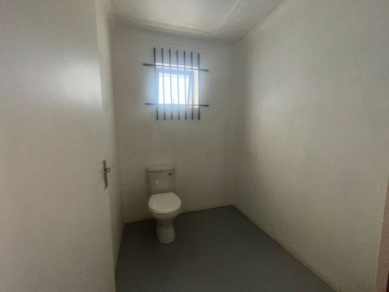 A basic industrial-style restroom featuring a single toilet and a small window secured with metal bars.
