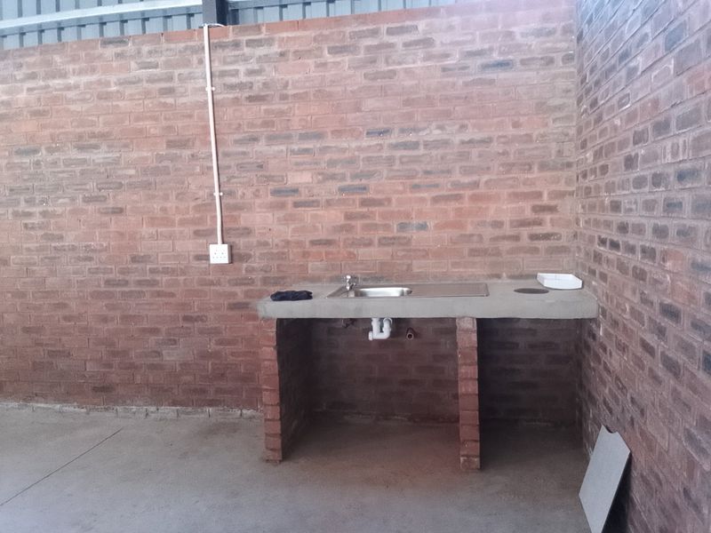 A functional utility space featuring exposed brick walls, a concrete countertop with an integrated stainless steel sink, and basic plumbing connections.