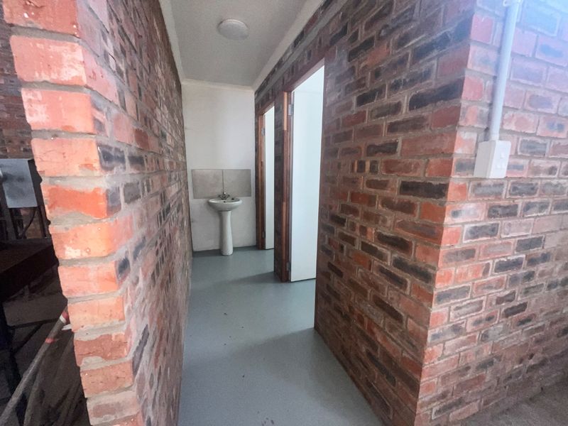 A functional hallway featuring exposed brick walls, a pedestal basin with a tiled splashback, and access to adjacent rooms.