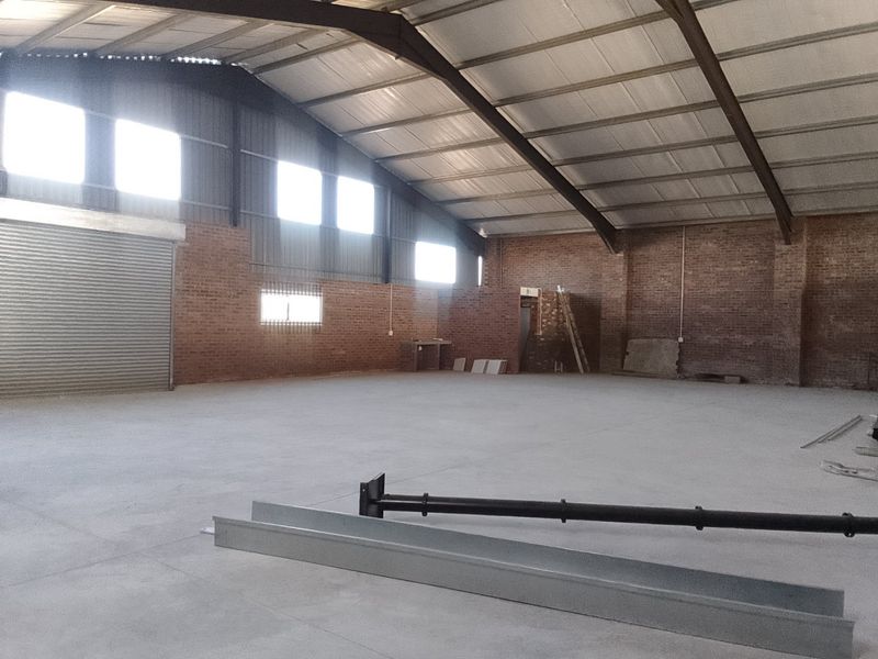 Spacious industrial warehouse featuring exposed brick walls, concrete flooring, and a high-clearance steel portal frame structure with a large roller shutter door.