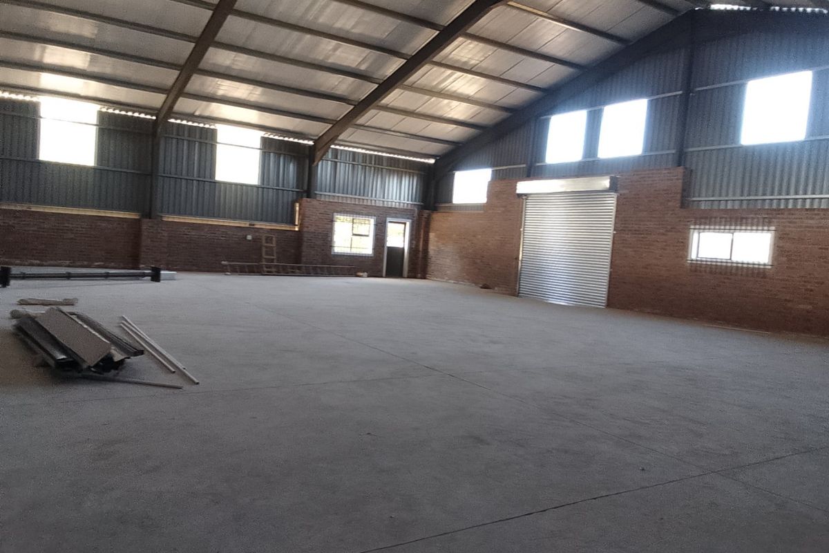 Spacious industrial warehouse featuring concrete flooring, exposed brick walls, and a large metal roller shutter door, suitable for various commercial or storage applications.