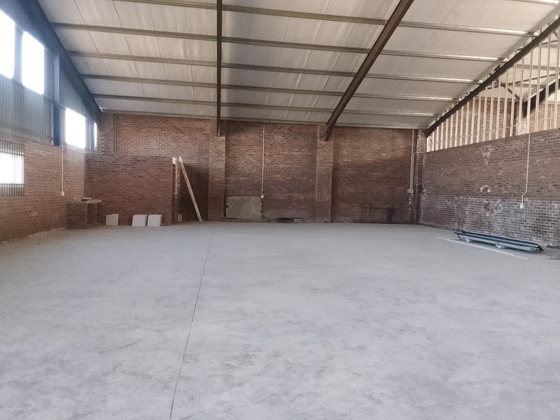 Spacious industrial warehouse interior featuring exposed brick walls, concrete flooring, and a high-clearance steel portal frame structure.