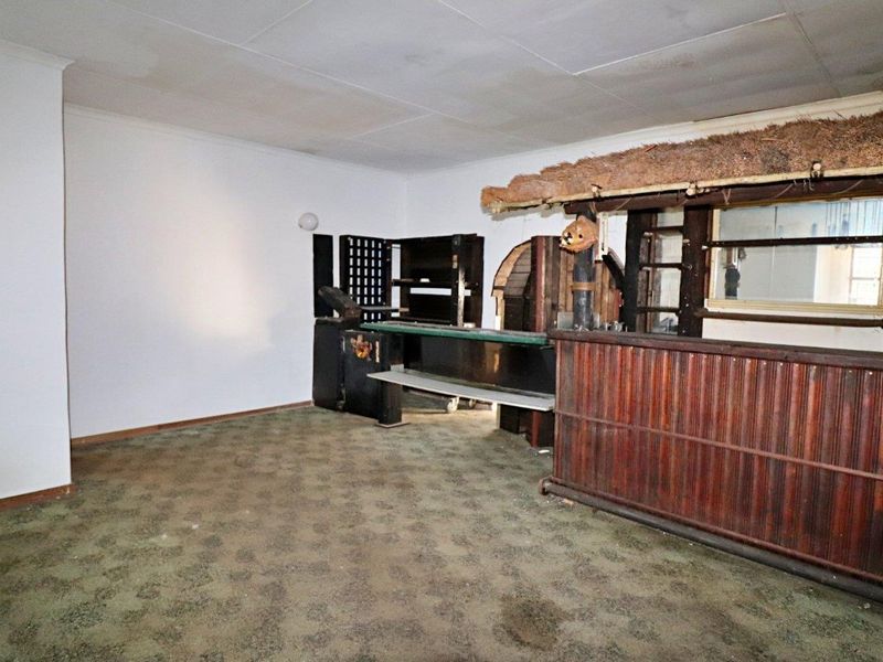 A dated bar area featuring a built-in counter, shelving, and a thatched roof detail, requiring significant cosmetic updates and flooring replacement.