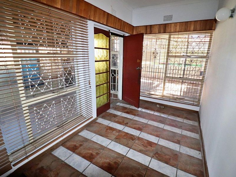 An empty entrance area featuring tiled flooring, timber wall paneling, and security features including a gate and window bars.