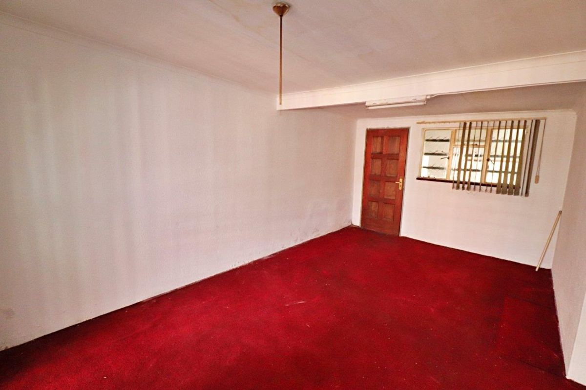 An empty bedroom featuring red carpet flooring, a timber door, and a window fitted with security bars.