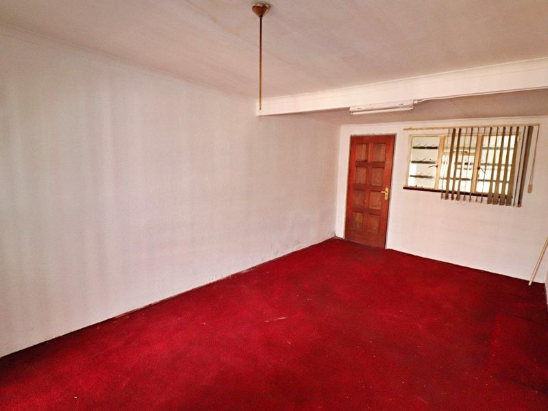 An empty bedroom featuring red carpet flooring, a timber door, and a window fitted with security bars.