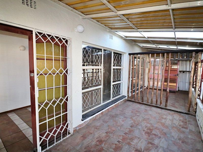 A covered patio area featuring tiled flooring, security gates, and a translucent roof structure, offering a functional outdoor space.