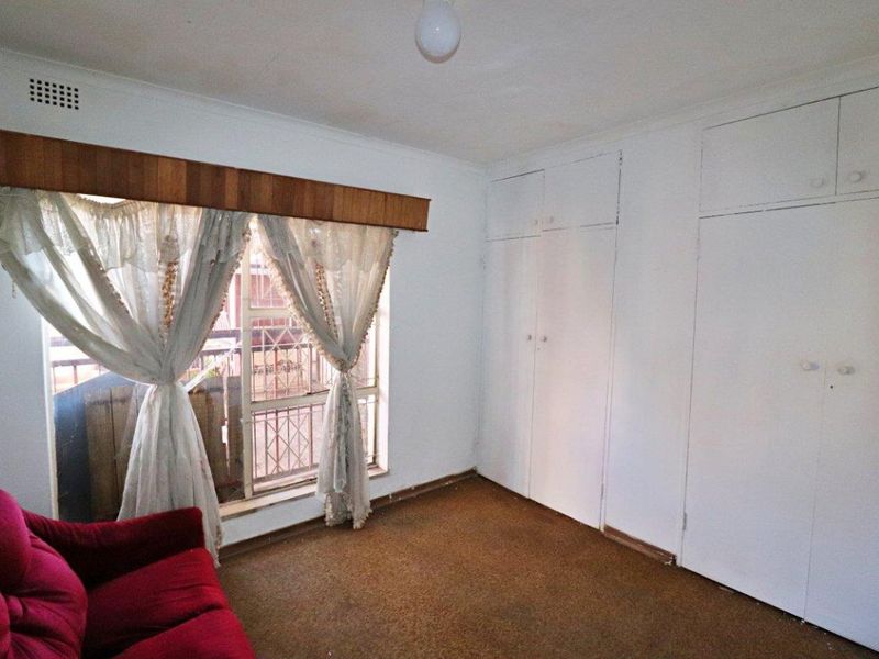 Bedroom featuring built-in cupboards, carpeted flooring, and window security bars. The space offers a functional layout with potential for modernization.