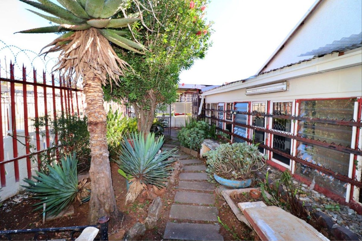 A narrow rear garden pathway featuring paved stones, established landscaping, and security-fitted windows along the side of the house.