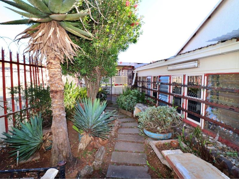 A narrow rear garden pathway featuring paved stones, established landscaping, and security-fitted windows along the side of the house.