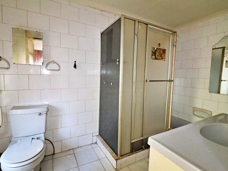 A dated bathroom featuring a shower enclosure, toilet, and vanity basin with wall-to-wall tiling, offering potential for a modern renovation.