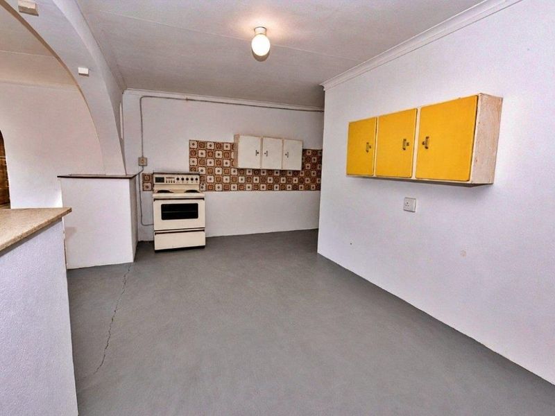 A dated, empty kitchen area featuring a freestanding stove, wall-mounted cabinets, and a tiled backsplash, requiring modernization and floor repairs.