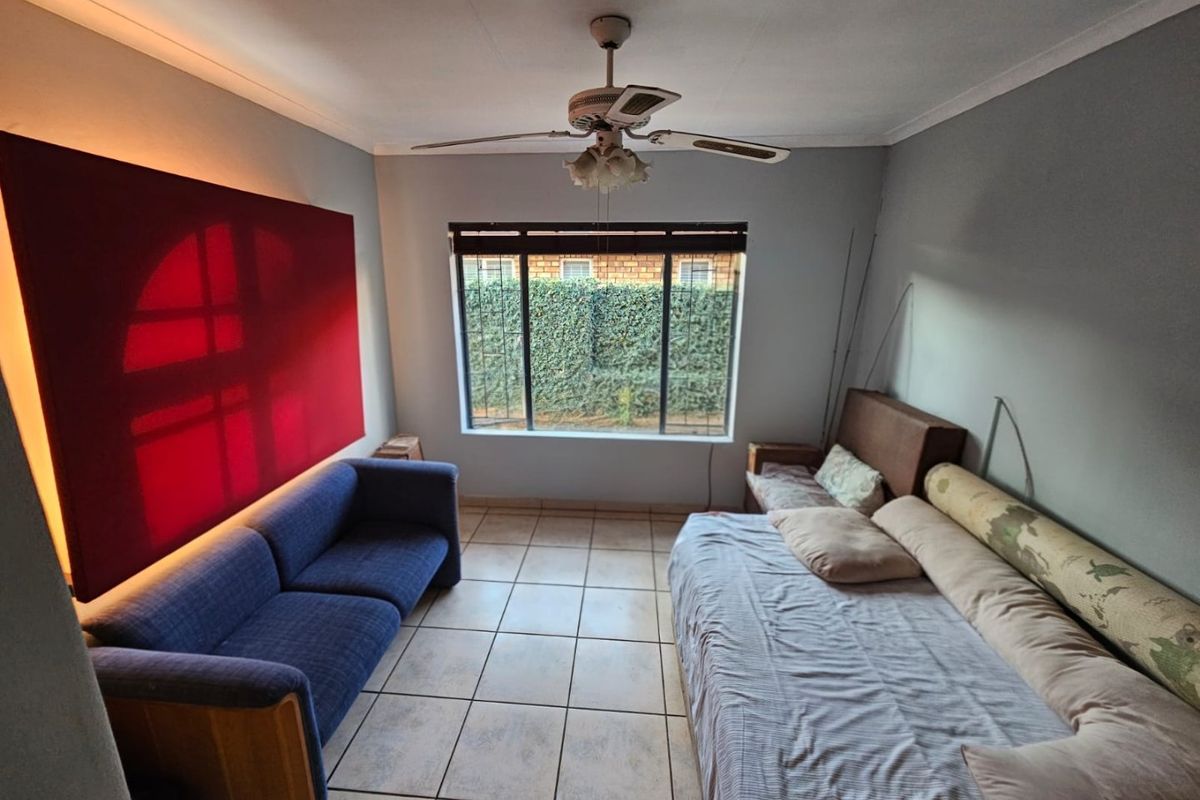 A bedroom featuring tiled flooring, a ceiling fan, and a window with security bars, offering a functional space with neutral wall finishes.