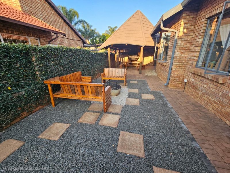 A private rear courtyard featuring brick paving, gravel landscaping, and a covered thatched gazebo area, ideal for outdoor relaxation.