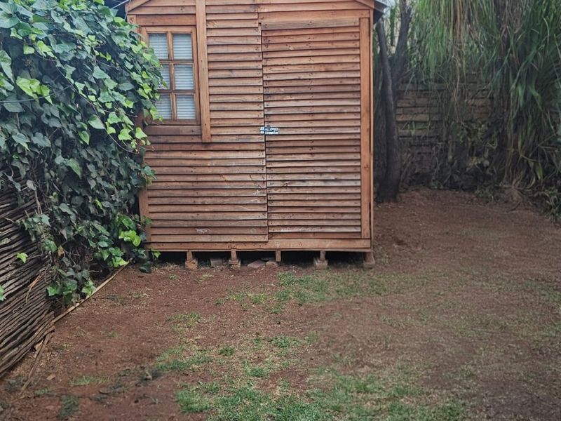 A backyard garden area featuring a wooden storage shed, paved patio section, and established perimeter fencing.