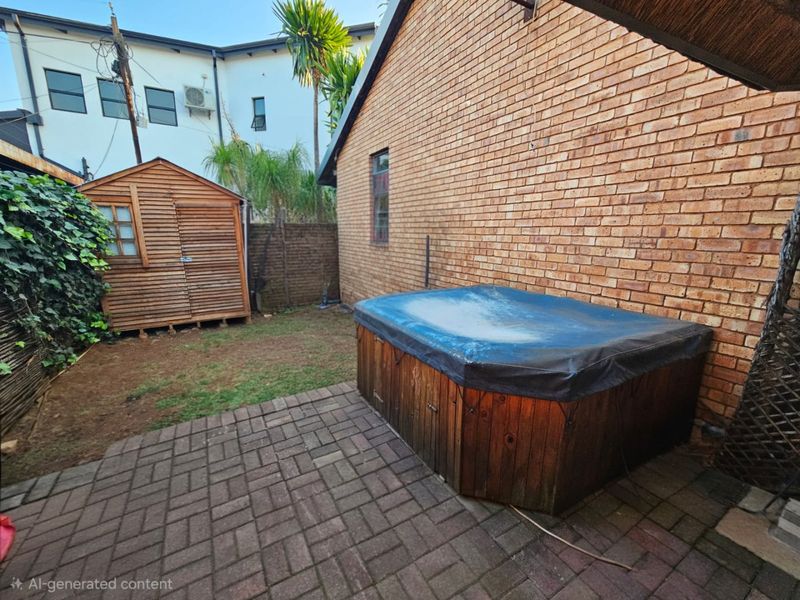 Rear courtyard area featuring brick paving, an exposed brick wall, a wooden garden shed, and a covered hot tub.