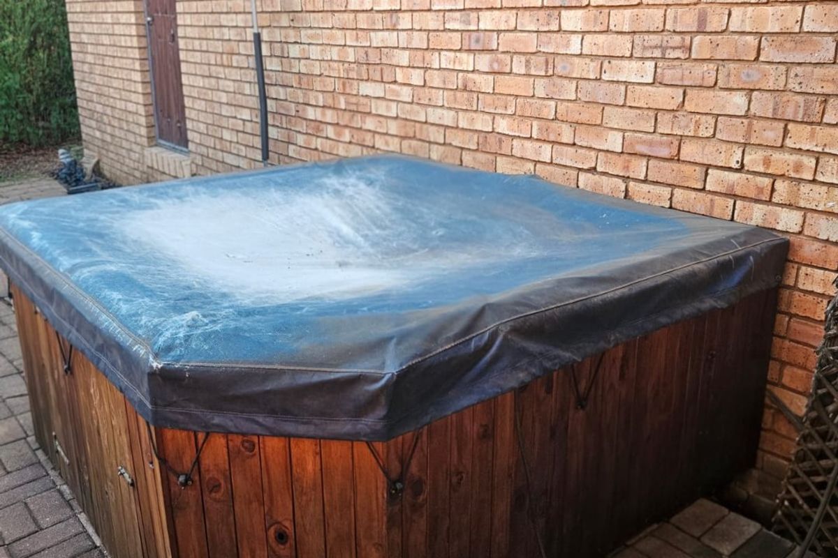 A rear exterior area featuring a brick wall and a covered hot tub set on a paved patio surface.
