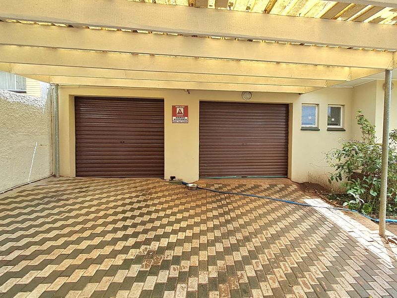 A double garage with roller doors and a covered carport area featuring paved flooring and security windows.