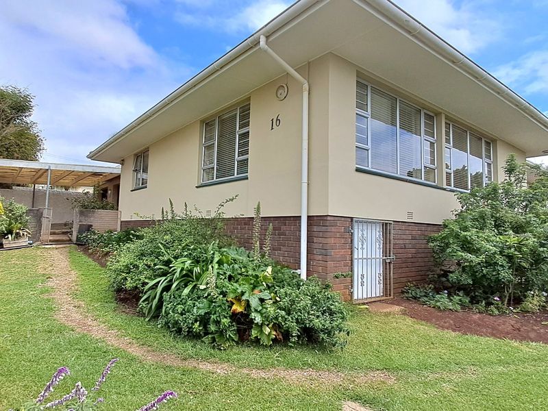 Front elevation of a well-maintained house featuring a brick base, plastered walls, and established garden surroundings.