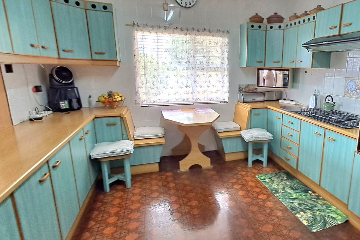 A dated kitchen featuring teal built-in cabinetry, a gas hob with extractor, and a built-in breakfast nook area with vinyl flooring.