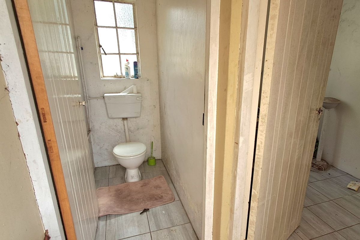 A small, dated bathroom featuring tiled flooring and a standard toilet, requiring significant cosmetic updates and wall repairs.